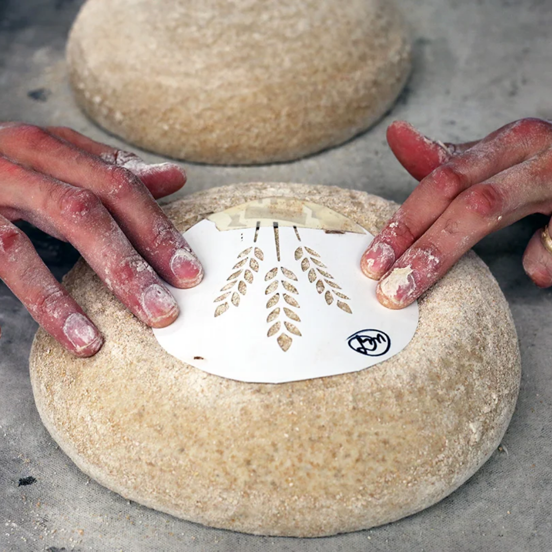 Hands pressing a white stamp with a design onto a round piece of dough.