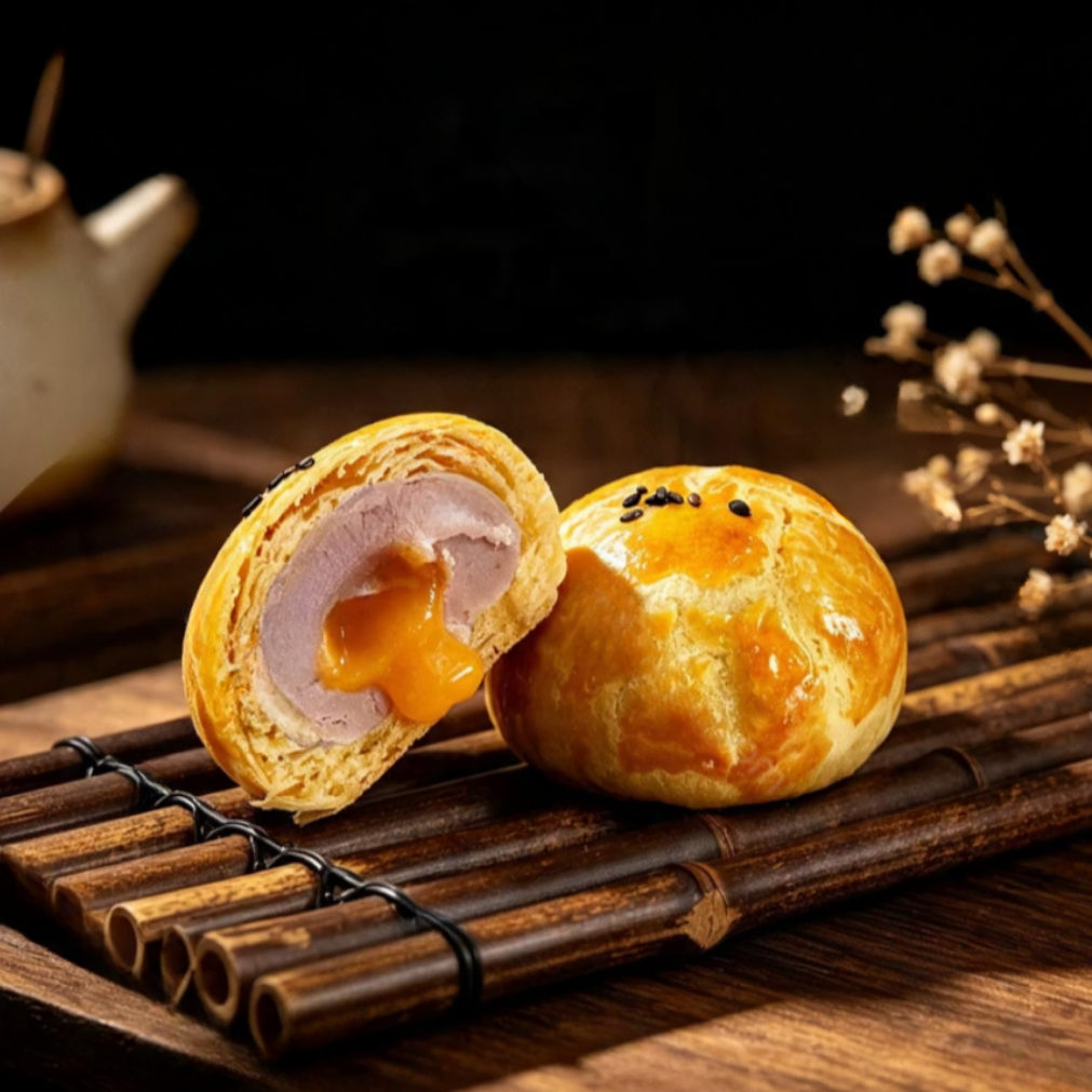 Golden flaky taro pastries on a bamboo mat, one cut open to reveal purple taro paste and a flowing salted egg lava centre