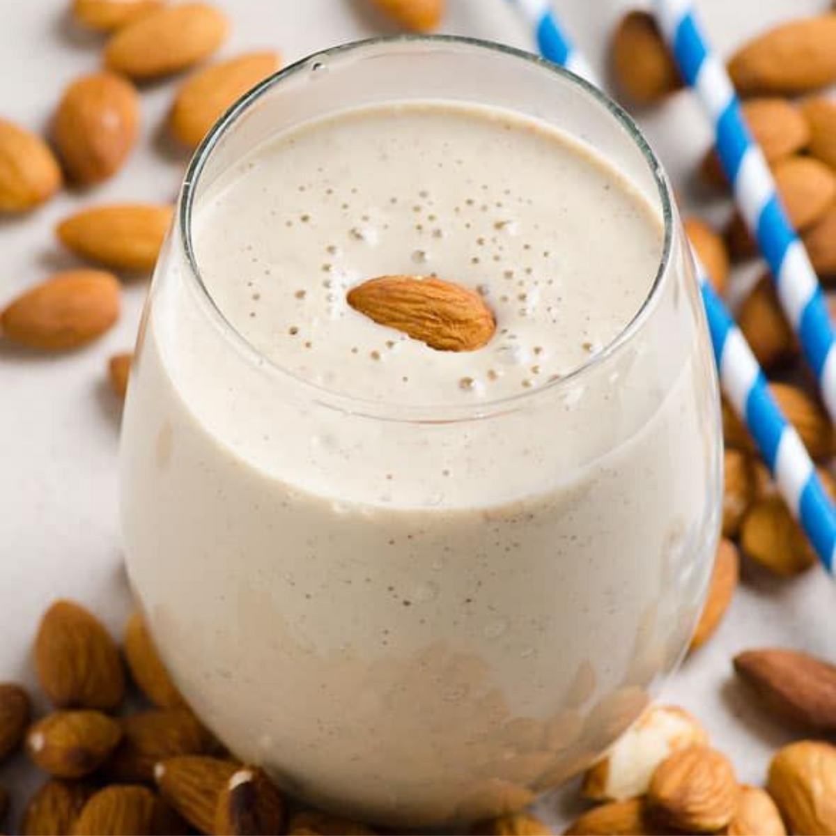 Creamy almond drink in a glass, topped with a whole almond and surrounded by almonds
