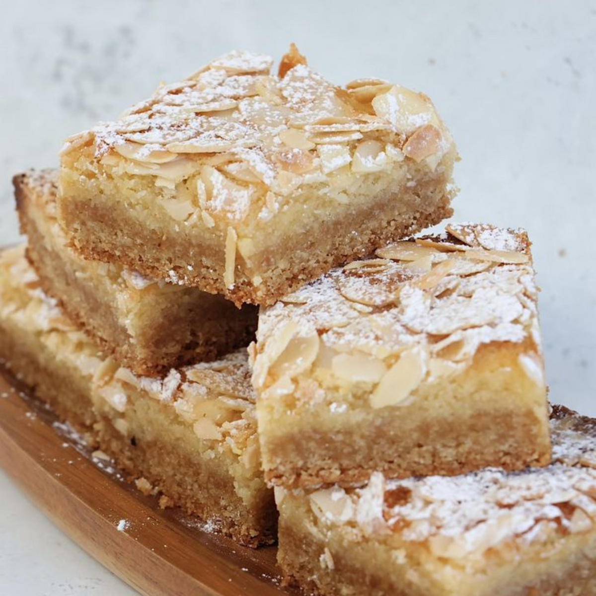 Stacked almond slices topped with flaked almonds and dusted with icing sugar on a wooden board