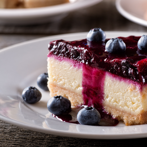 Cheesecake slice topped with blueberry sauce and fresh blueberries on a white plate