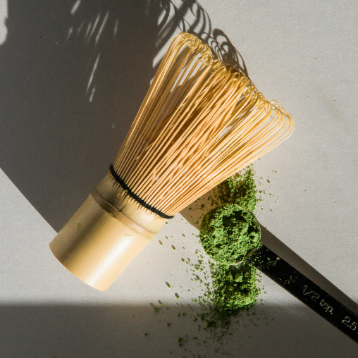 Bamboo tea whisk beside a measuring spoon and scattered green tea powder