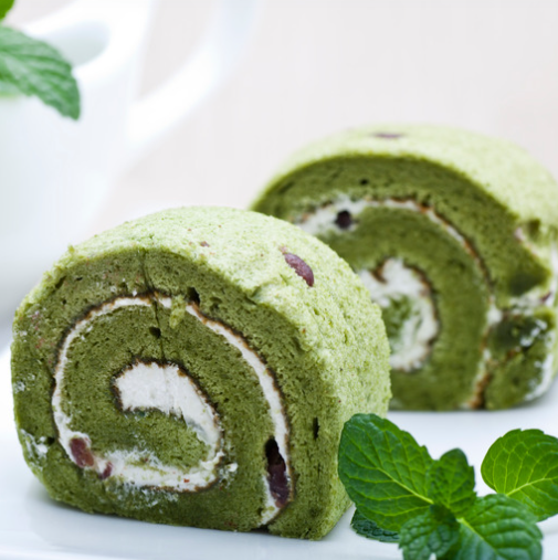 Green tea Swiss roll slices with cream filling and mint leaves on a white plate