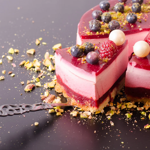 Pink layered berry mousse cake with a red glaze, fresh berries and chopped nuts