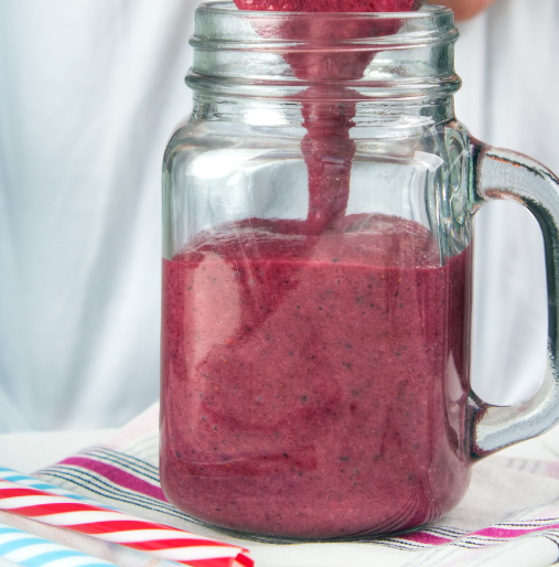 Thick pink fruit smoothie being poured into a handled glass jar