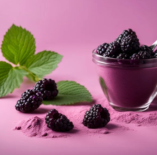 Purple berry dessert in a glass cup topped with blackberries, beside berry powder and green leaves