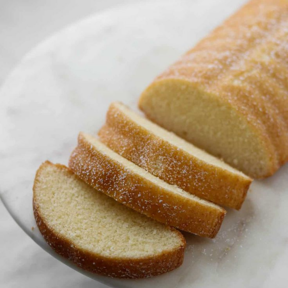 Golden loaf cake with three slices on a white plate, lightly dusted with icing sugar